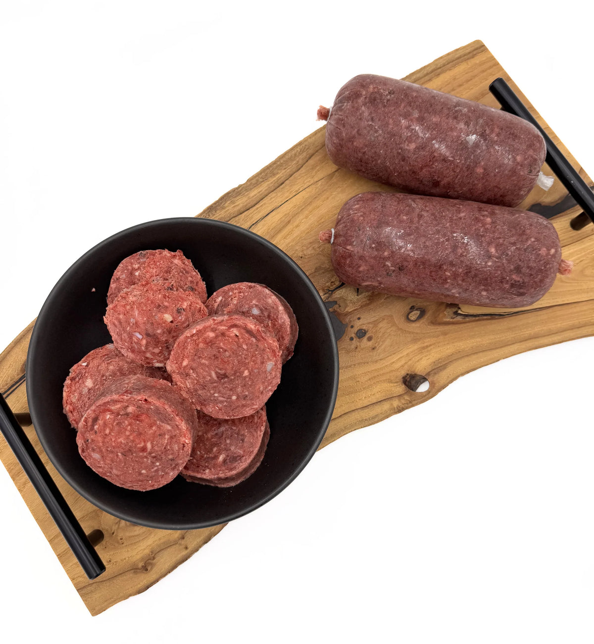 Raw pet food on a wooden board with a black bowl containing sliced sausages.