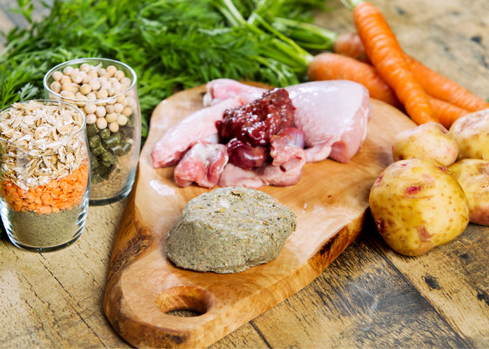 Chicken raw dog food on a cutting board with carrots and potatoes